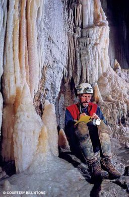 Mustached man sits down in a cave to take notes