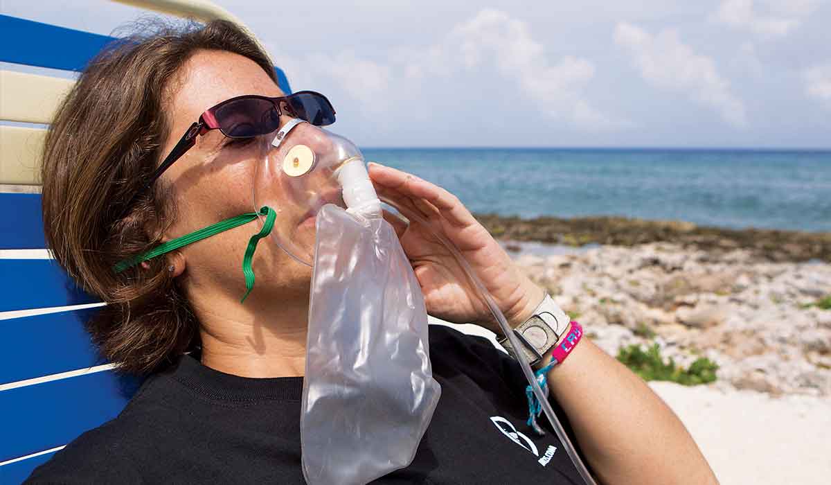 Woman lies in beach chair wearing oxygen mask