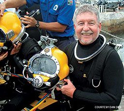 Bearded man in a scuba suit holds a yellow helmet