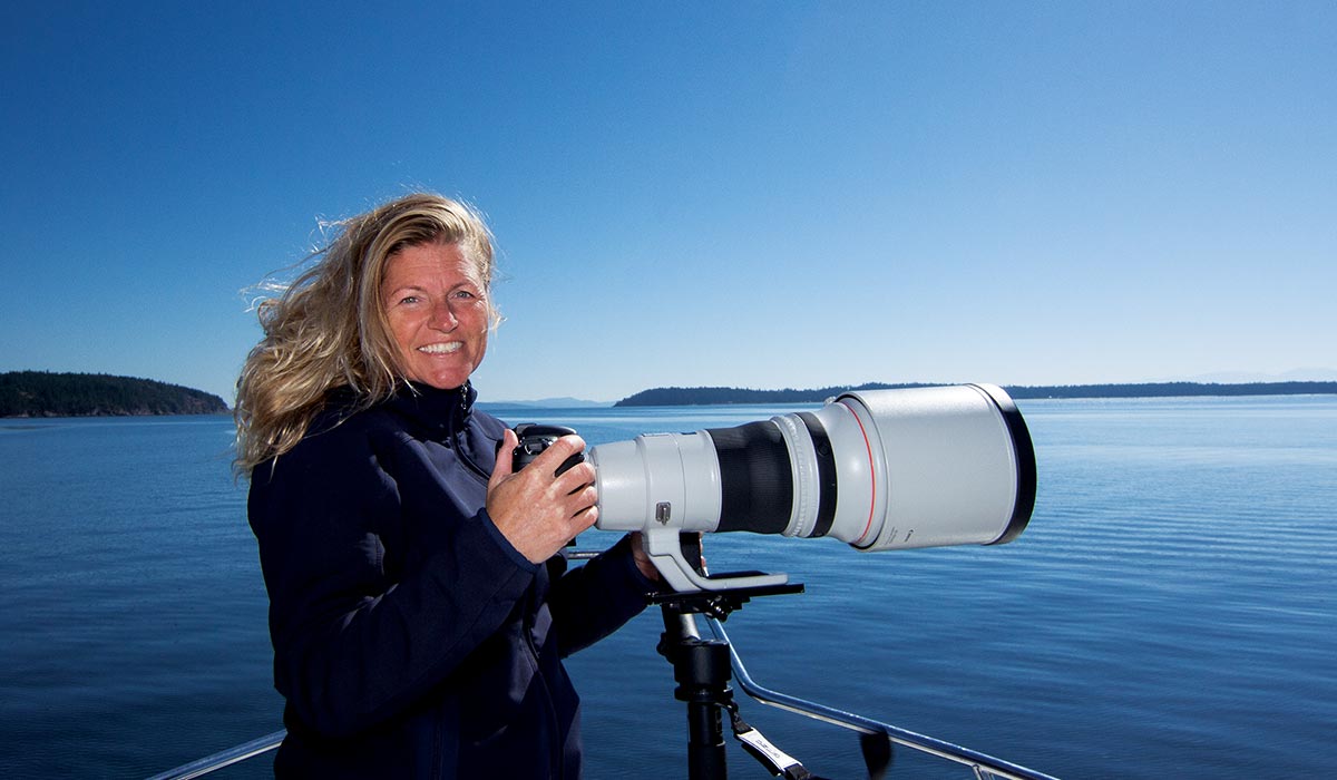 Blonde woman stands behind camera with a long lens