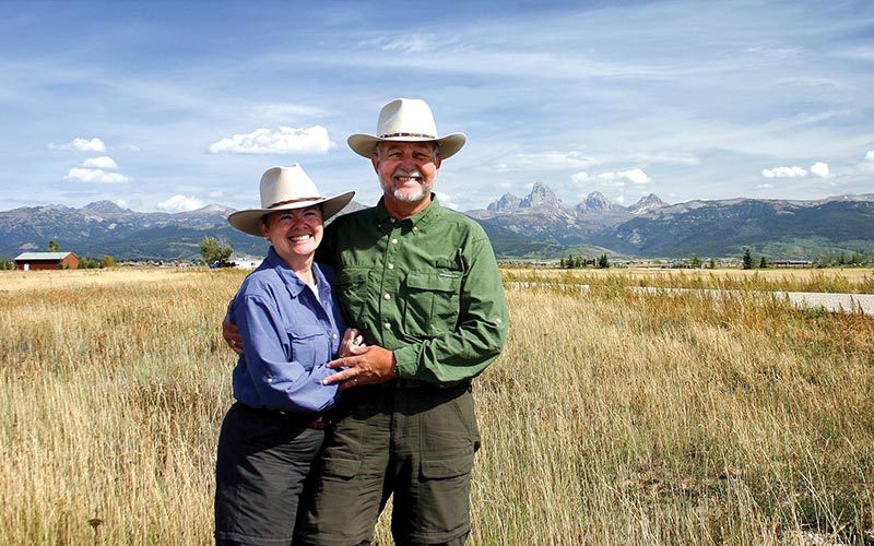 Woman and man wear cowboy hats and stand in field