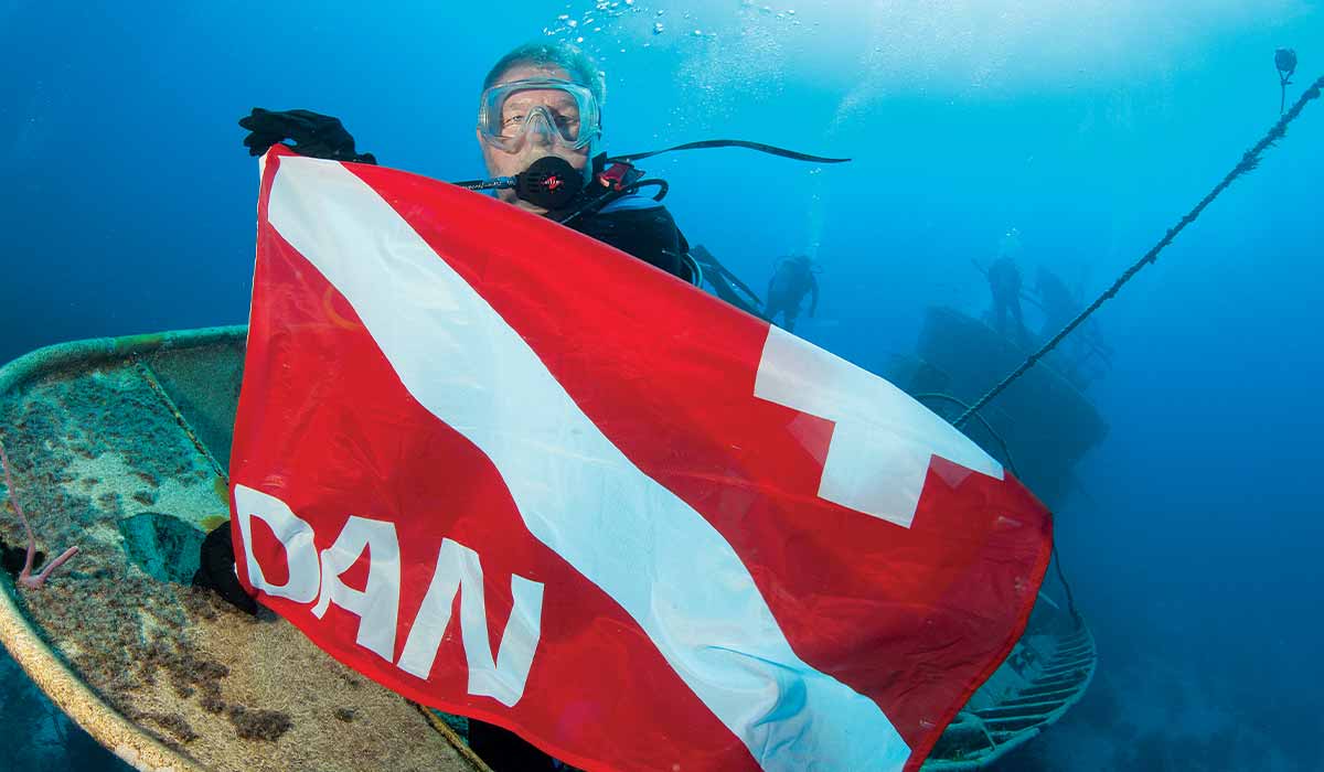 Scuba diver Dan Orr is submerged and holding a red DAN flag