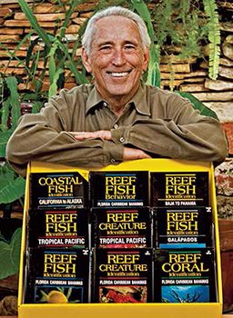 Headshot of Ned DeLoach and he is posing with a yellow display of his books