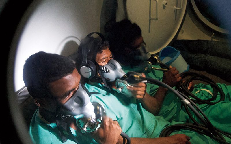 Three divers in hyperbaric chamber using oxygen masks