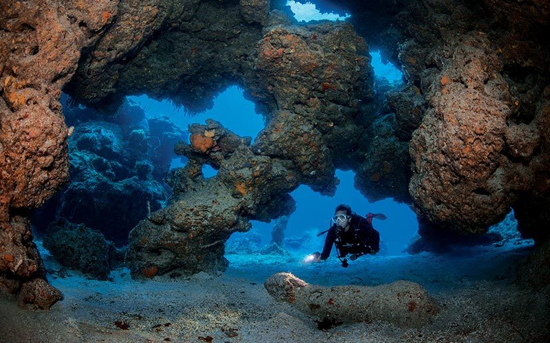 Diver swims through underwater cave formations