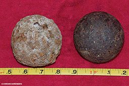 Two recovered cannon balls are on red background and behind measuring tape
