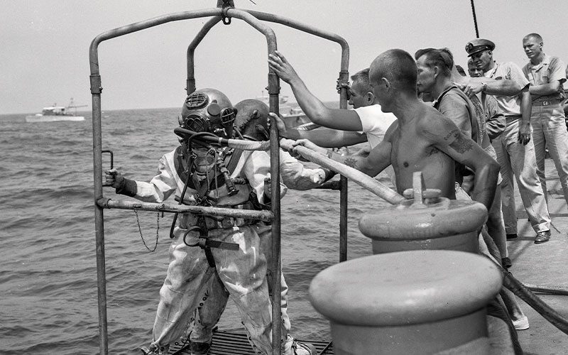 Old black-and-white image of divers being lowered into water