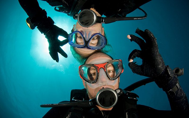 A male and female diver each give the camera the OK sign