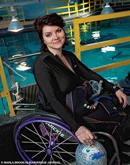 Headshot of Cody Unser in a scuba suit, sitting in a purple-rimmed wheelchair and holding a globe in her right hand