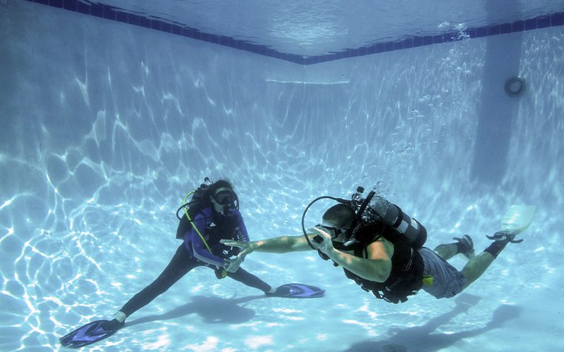 Two divers practice diving in a pool