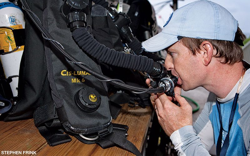 A diver performs a predive check to confirm proper gear function.