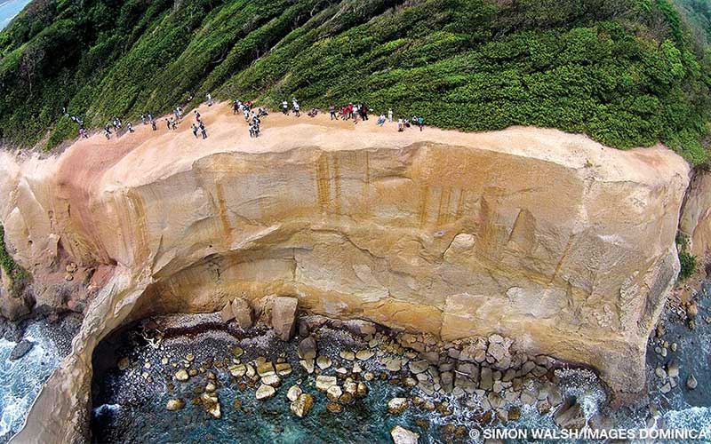 This overhead drone photo shows tiny humans on top of a coastal rock wall