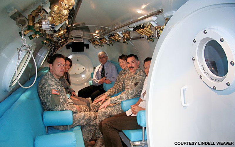 U.S. Department of Defense hyperbaric brain injury research staff gather in a chamber at a military study site.