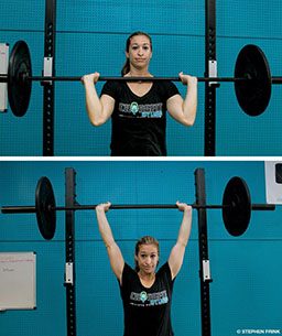 A woman in teal shorts performs the proper technique for the barbell military press