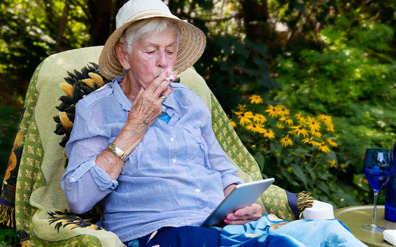 Old woman in a straw hat is smoking a cigarette in her garden