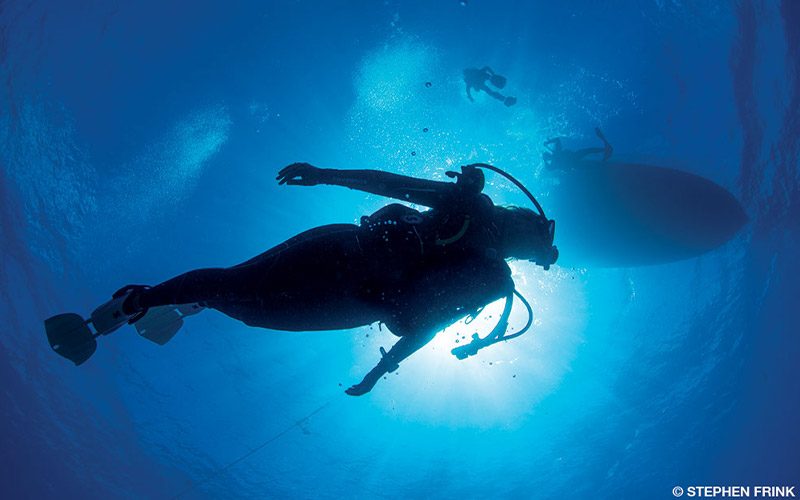 Woman dives beneath a boat