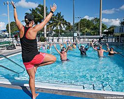A trainer, in pink shorts, leads a water aerobic class
