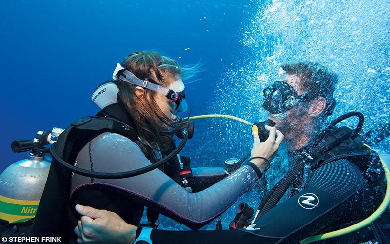 A female dive buddy gives her dive buddy the regulator so he can get air