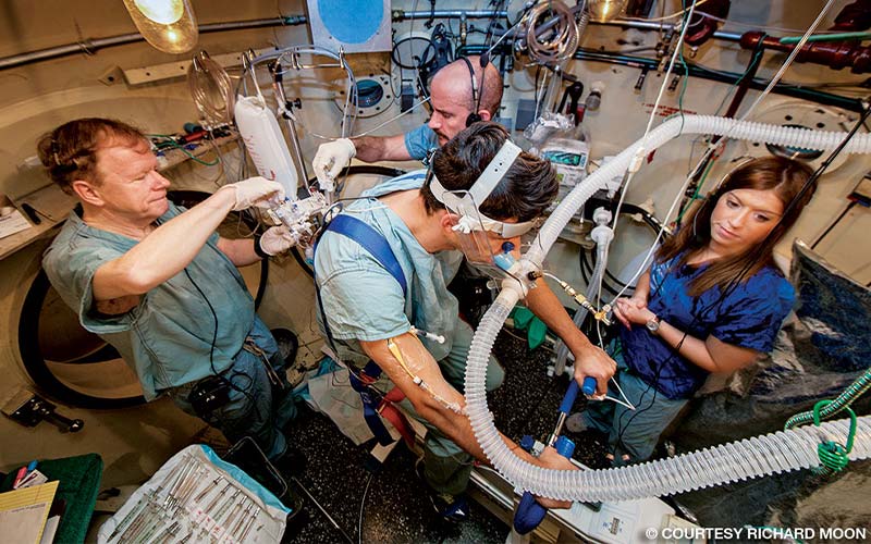 A group of researchers surround a man hooked up to tubes and machines.