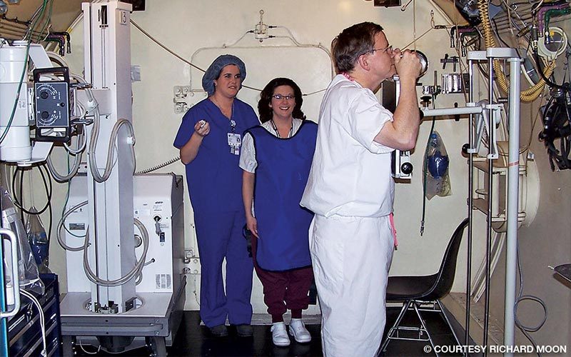 Richard Moon wears white scrubs and two female nurses are in the background