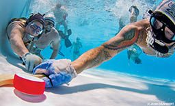 Swimmers play a raucous game of underwater hockey. The puck is bright red.