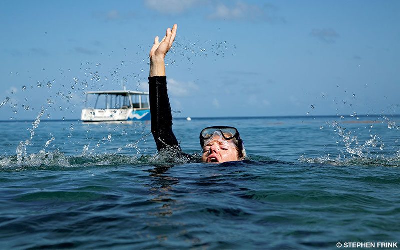 A female diver breaks the surface of the water. She's in shock and looks like she is in trouble.