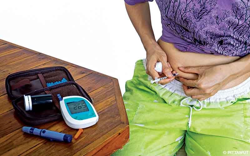 A person jabs their stomach with insulin. They are wearing green pants and a purple shirt.