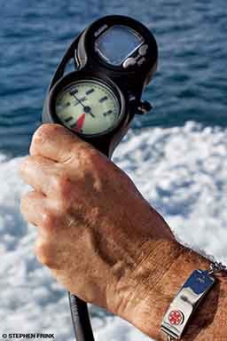 This is a close-up image of a man's hand. He's holding something and around his wrist is a Medic Alert bracelet. 