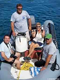 Three men and one woman are on a boat. The woman is giving two thumbs up.