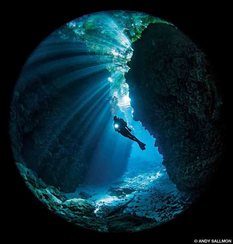 A cave diver explores a crevice and is lighted interestingly. 