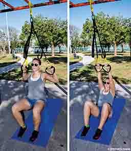 A female personal trainer demonstrates an assisted pull-up exercise via a suspension trainer.
