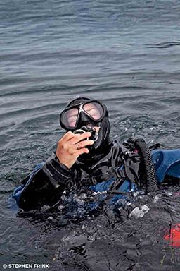 A diver has come up for air dramatically and his hand is on his regulator.