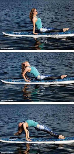 A personal trainer sits on a paddleboard and performs upward plank pose.
