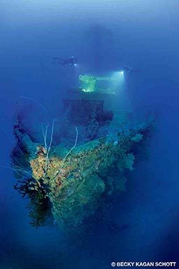 Two divers explore the outsides of a shipwreck.