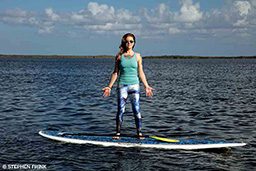 A personal trainer demonstrates mountain pose while standing on a paddleboard