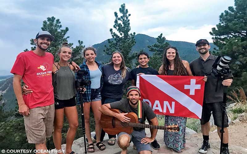 A group of high school students pose with several adults. Mountains are in the background.