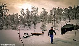 A man walks through the snowy ground. A snowmobile is behind him