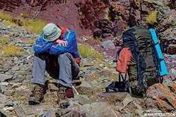 A hiker sits down because he has altitude sickness and is uncomfortable. 