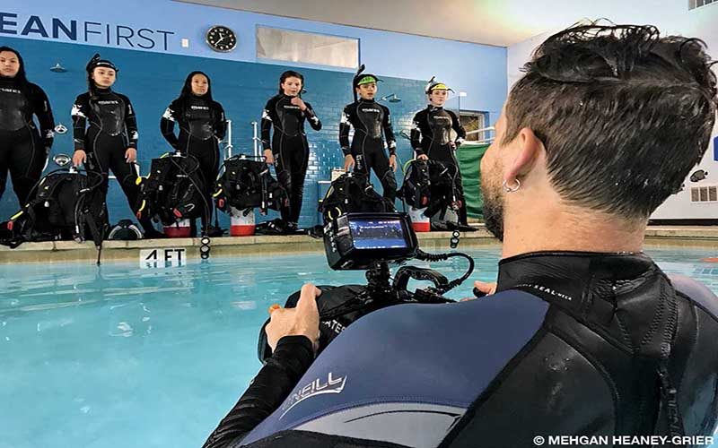 Six students in dive gear, stand on the pool deck.