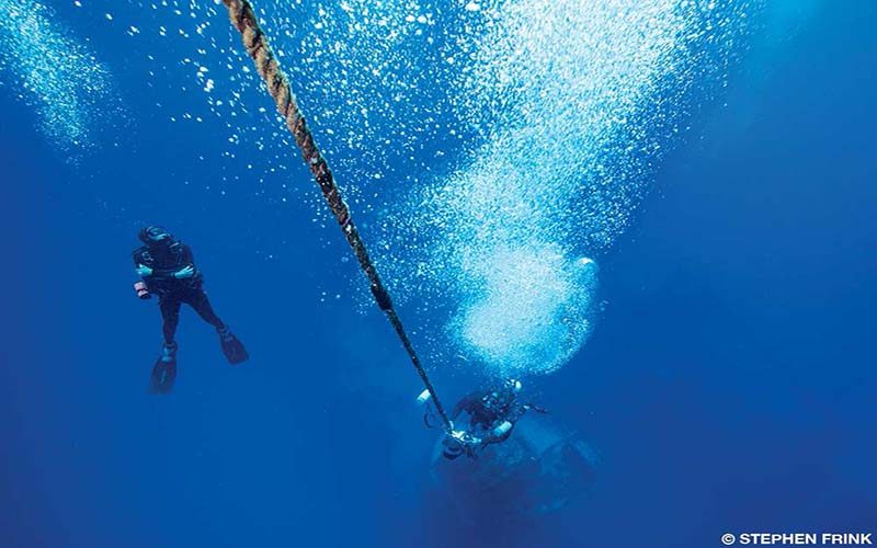 Two divers swim below and there are a lot of bubbles around them.