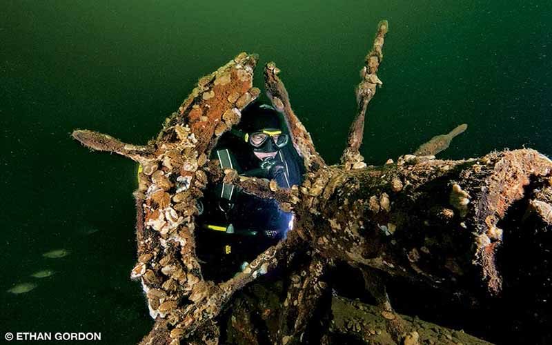 Diver Lars Brinkmann illuminates the old wooden ship’s wheel on the wreck of the O.J. Walker, one of 10 historic shipwrecks preserved in Lake Champlain.