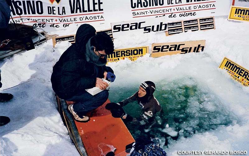 Dr. Bosco kneels on icy land next to diver in the ice