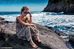 A woman sits on a rock and is worried. She has anxiety.