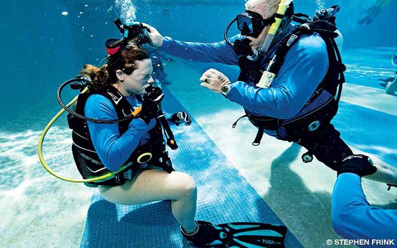 A female diver receives assistance from a male diver