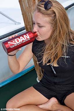 A woman takes a drink from a red DAN waterbottle