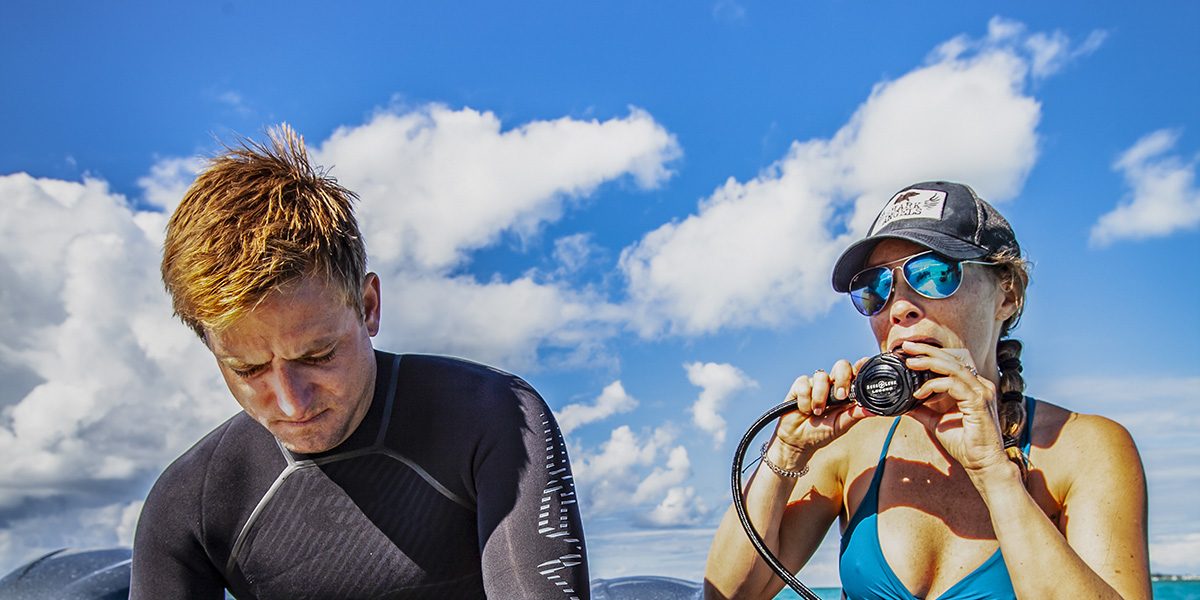 a male and female diver check their regulator and other equipment as they prepare to dive