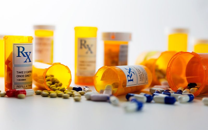 Several prescription bottles, some lying down with pills scattered, rest on a white backdrop