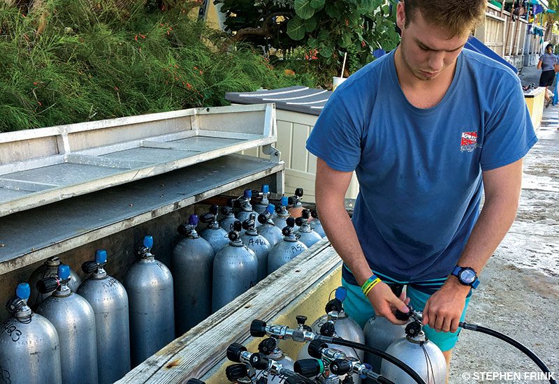 Young man in blue shirt fills scuba cylinders.