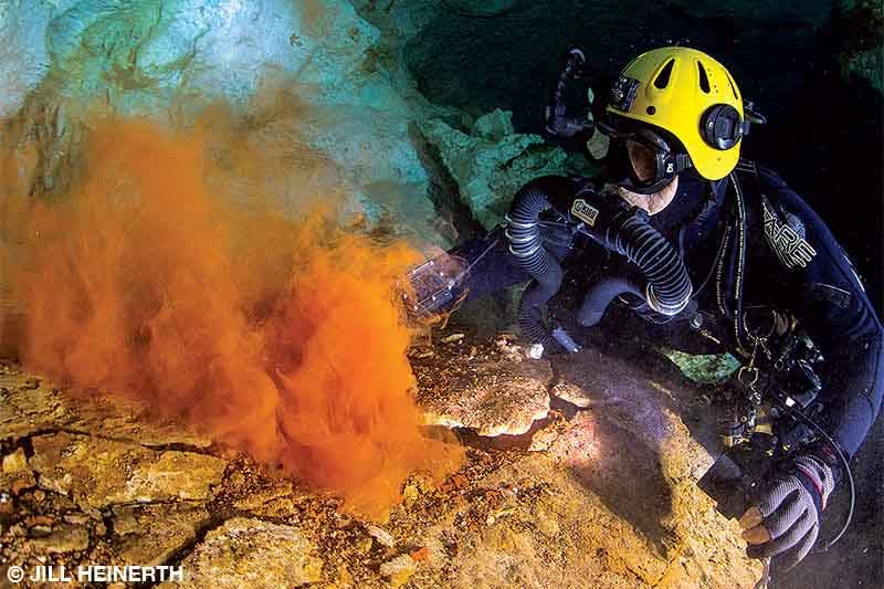 A diver watches dust rise from layers of rock underwater in a cave in the Bahamas.