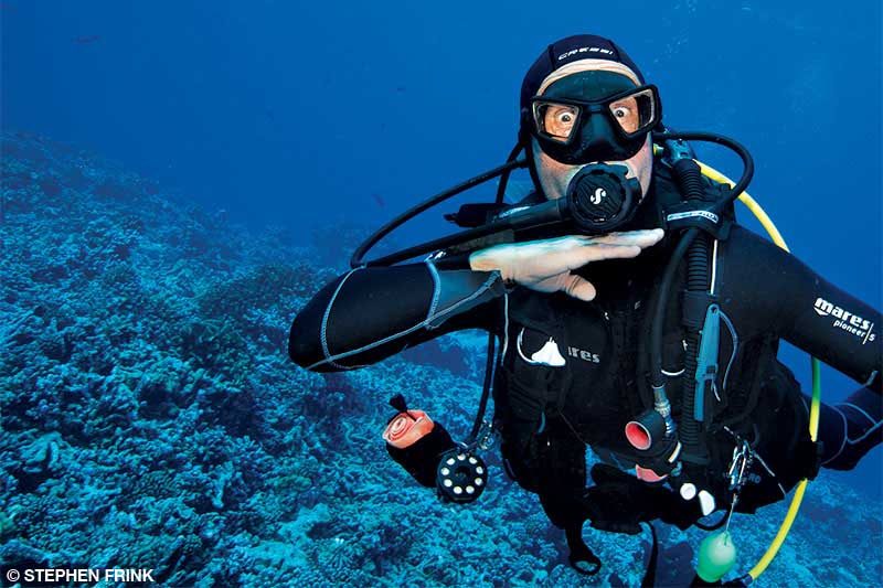 A diver underwater gives an out of air signal by putting his hand across his throat.